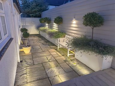 A patio area with stone paving white bench potted plants and wall lighting at Ty Coed in Abersoch