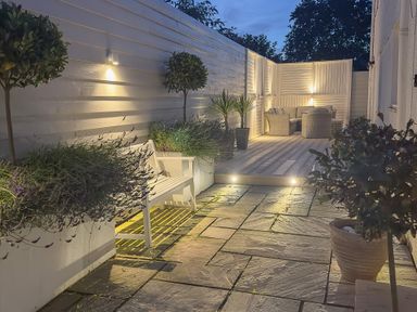 An outdoor patio area with stone flooring white bench plants and a seating area with wicker furniture at Ty Coed in Abersoch