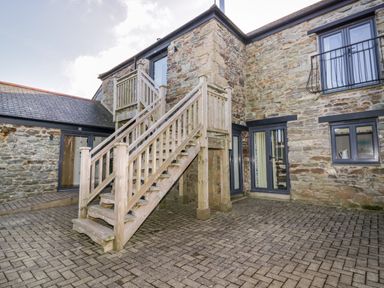 An outdoor courtyard with stone walls wooden staircase and multiple windows at Beacon Barn in St Agnes