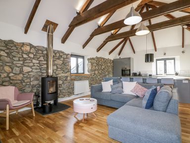 A living room with a grey sofa pink armchair wood burning stove and exposed stone walls at Beacon Barn in St Agnes