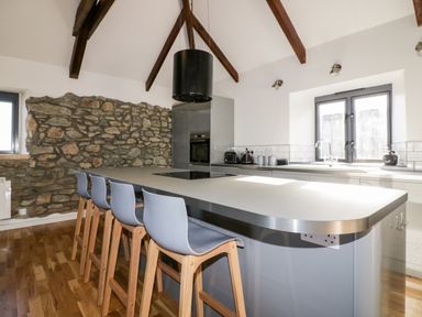 A kitchen with stone wall beams island counter with stools and windows at Beacon Barn in St Agnes