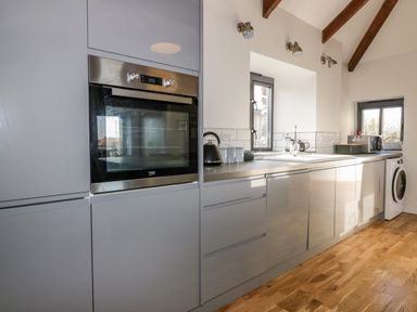 A kitchen with grey cabinets an oven a washing machine and a sink under a window at Beacon Barn in St Agnes