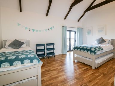 A bedroom with two single beds two small shelves and a window with light blue curtains at Beacon Barn in St Agnes
