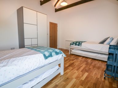 A bedroom with two single beds wooden floor wardrobe and a wooden door at Beacon Barn in St Agnes