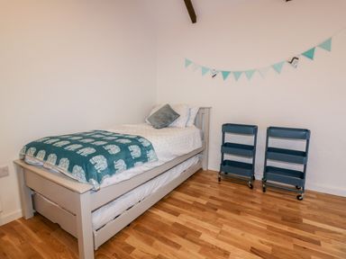 A bedroom with a single bed with a pull-out trundle bed and two metal rolling storage carts on a wooden floor at Beacon Barn in St Agnes
