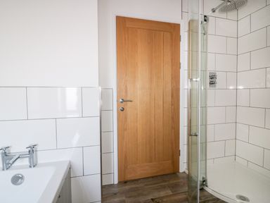 A bathroom with a wooden door a sink with faucet and a glass shower enclosure with tiled walls at Beacon Barn in St Agnes