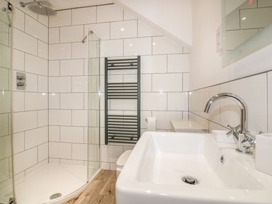 A bathroom with a glass shower enclosure a white sink with a chrome faucet a black heated towel rail and a toilet at Beacon Barn in St Agnes