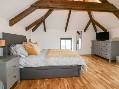 A bedroom with a large bed bedside tables wooden beams on ceiling a dresser with a television and a mirror on the wall at Beacon Barn in St Agnes
