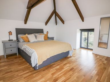 A bedroom with a bed with pillows and blankets two bedside tables with lamps a window and a mirror on the wall at Beacon Barn in St Agnes