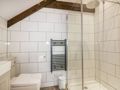 A bathroom with a toilet, a towel radiator, a trash bin, and a glass shower enclosure at Beacon Barn in St Agnes