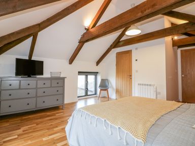 A bedroom with wooden floor beams a dresser a television a chair and a bed at Beacon Barn in St Agnes