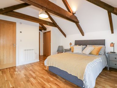 A bedroom with a double bed pillows bedside tables wooden beams on the ceiling and wooden doors at Beacon Barn in St Agnes