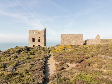 Stone ruins on a hill with bushes and a path leading to them at Beacon Barn in St Agnes
