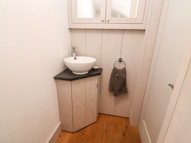 A small bathroom corner with a round sink on a black countertop a towel hanging on a ring and wooden floor at Stow Cottage Barn in Churchill Oxfordshire