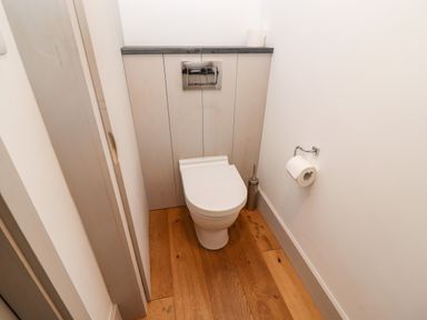 A small bathroom with a white toilet a toilet brush holder and a toilet paper holder on a wooden floor at Stow Cottage Barn in Churchill Oxfordshire