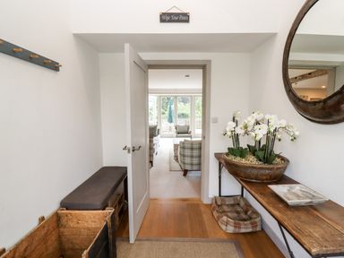 An entryway with a wooden bench and storage boxes a door leading to a living room with armchairs a wooden table with a flower arrangement and a pet bed below at Stow Cottage Barn in Churchill Oxfordshire