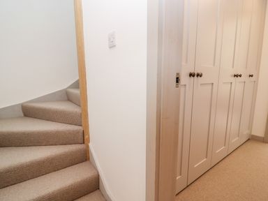 A carpeted staircase next to white built-in cupboards with wooden knobs at Stow Cottage Barn in Churchill Oxfordshire