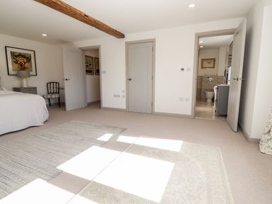 A bedroom with a bed a chair two rugs and open doors showing a bathroom at Stow Cottage Barn Churchill Oxfordshire