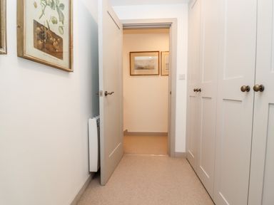 A hallway with a partially open door cabinets on one side and framed pictures on walls at Stow Cottage Barn in Churchill Oxfordshire