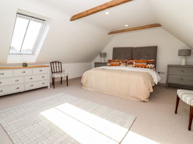 A bedroom with a double bed, two grey bedside cabinets with lamps, a chest of drawers, two wooden chairs, and a window on a slanted ceiling at Stow Cottage Barn in Churchill Oxfordshire