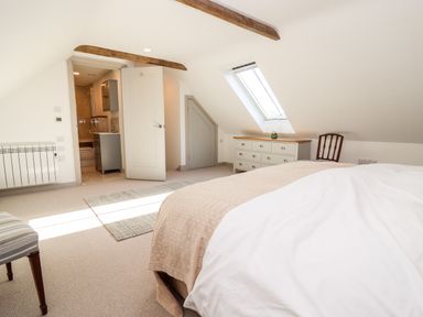 A bedroom with a bed a chest of drawers a chair and an open door leading to a bathroom at Stow Cottage Barn in Churchill Oxfordshire