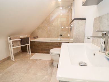 A bathroom with a bathtub with glass shower screen a toilet a white sink and towels on a rack at Stow Cottage Barn in Churchill Oxfordshire