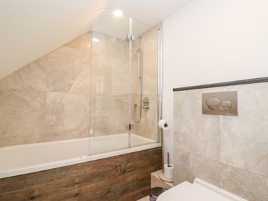 A bathroom with a bathtub featuring a glass shower screen and tiled walls at Stow Cottage Barn in Churchill Oxfordshire