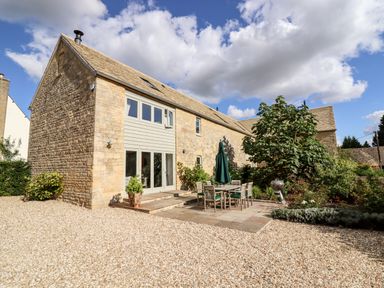 Stone house with a patio set and umbrella outside and gravel driveway at Stow Cottage Barn in Churchill Oxfordshire