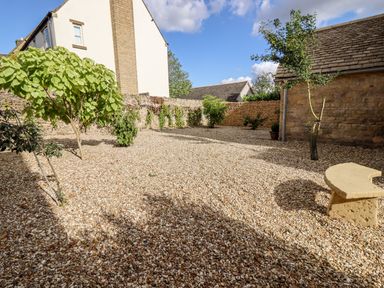 A garden area with small trees and gravel ground surrounded by stone walls at Stow Cottage Barn Churchill Oxfordshire