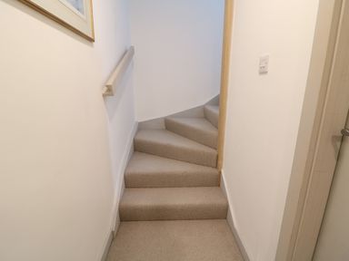 A carpeted staircase with a handrail on the left wall and a light switch on the right wall at Stow Cottage Barn in Churchill Oxfordshire