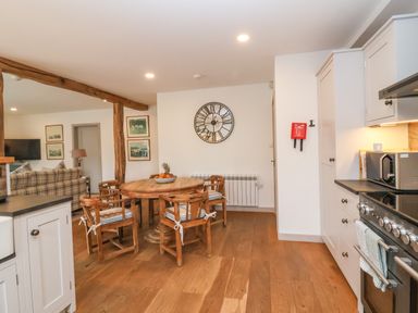 A kitchen and dining area with a round wooden table and four chairs wooden flooring and white cabinetry at Stow Cottage Barn in Churchill Oxfordshire