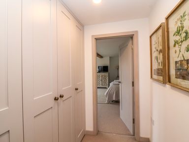 A hallway with closed cabinets on the left and floral framed artwork on the right leading to a bedroom at Stow Cottage Barn in Churchill Oxfordshire
