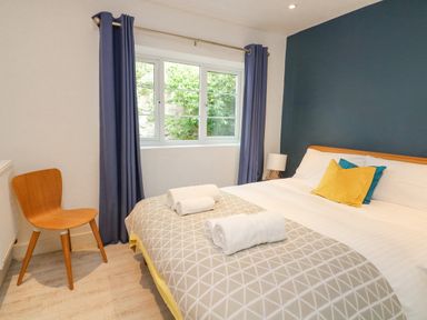 A bedroom with a bed with pillows and folded towels a wooden chair near a window with blue curtains at Landmark in Salcombe