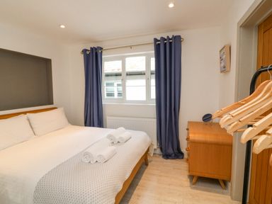 A bedroom with a double bed, blue curtains, a wooden dresser, and wooden hangers on a rack at Landmark in Salcombe