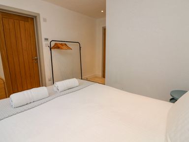 A bedroom with a bed, rolled towels on the bed, a clothes rack with hangers, wooden doors, and plain walls at Landmark in Salcombe