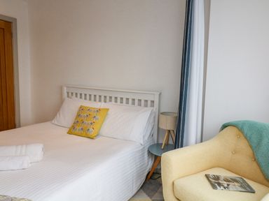A bedroom with a white bed with a yellow cushion and folded towels next to a yellow armchair with a magazine and a green blanket at Landmark in Salcombe