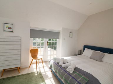 A bedroom with a bed a wooden chair a white cabinet and glass doors at Landmark in Salcombe