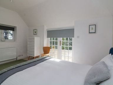 A bedroom with a white bed a wooden chair a white dresser and glass doors with gray blinds at Landmark in Salcombe