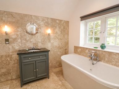 A bathroom with a bathtub and a vanity unit with sink under a round mirror at Landmark in Salcombe