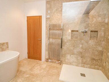 A bathroom with a wooden door a white bathtub a chrome towel radiator and a tiled shower area at Landmark in Salcombe