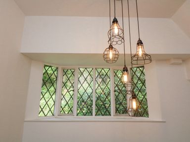A window with diamond-patterned panes and hanging wire cage light fixtures at Landmark in Salcombe