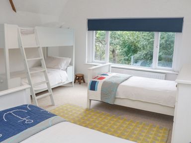 A bedroom with bunk beds twin beds a small wooden stool and a large window with a blue blind at Landmark in Salcombe