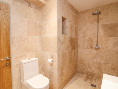 A bathroom with a toilet shower head and stone tiled walls at Landmark in Salcombe