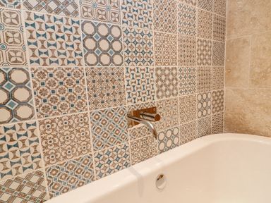 A bathtub with patterned tiles and a wall-mounted faucet at Landmark in Salcombe