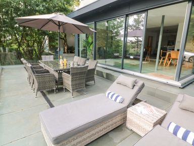An outdoor patio with lounge chairs and dining table under umbrella next to glass sliding doors at Landmark Salcombe