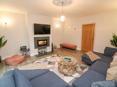 A living room with a blue sectional sofa a glass coffee table with stones a wall-mounted tv and a fireplace at Landmark in Salcombe