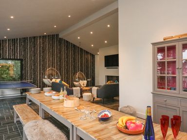A dining area with a long wooden table and benches adjacent to a living space with two gray sofas and hanging bubble chairs at Landmark in Salcombe