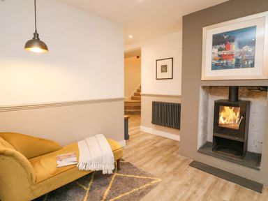 A room with a yellow chaise lounge blanket and magazine by a fireplace with fire and framed pictures at Landmark in Salcombe