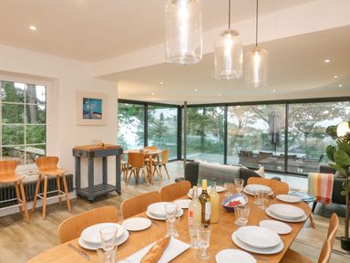A dining area with a wooden table set with plates glasses and bottles near a living space with large glass windows at Landmark in Salcombe