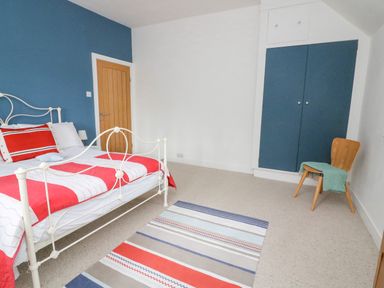 A bedroom with a white metal bed frame red and white bedding a wooden door blue wardrobes a wooden chair with a green throw and a striped rug on the floor at Landmark in Salcombe